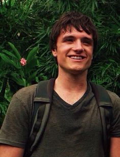 a man with a backpack standing in front of some plants and flowers smiling at the camera