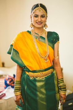 a woman in a green and yellow sari with gold jewelry on her head, standing next to a bed