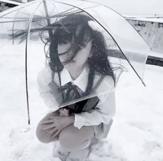 a woman kneeling in the snow with an umbrella over her head and hands on her knees