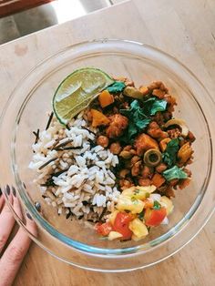 a glass bowl filled with rice, meat and veggies next to a lime