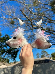 two small white dogs with pink bows on their head and ears are being held up by someone's hand