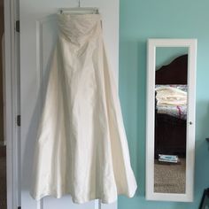 a wedding dress hanging on a door with a mirror in the corner and a bed behind it