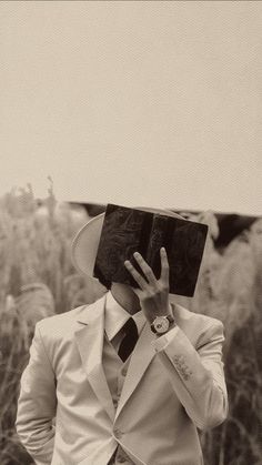 a man in a white suit and hat holds his hands up to his face as he looks at an open book