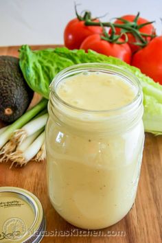 a wooden cutting board topped with a mason jar filled with liquid next to tomatoes and lettuce