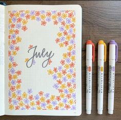 three markers and an open notebook with the word july written on it next to some pens