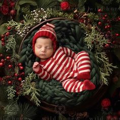 a baby in a red and white striped outfit sleeping on a green blanket surrounded by christmas greenery