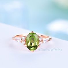 an oval green gemstone surrounded by white diamonds in a rose gold ring on a blue background