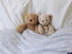 two teddy bears are laying in bed together