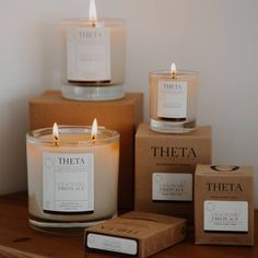 three candles sitting on top of a wooden table next to boxes with labels and soaps