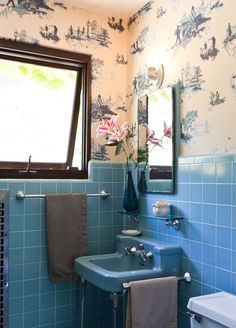 a bathroom with blue tile and wallpaper has a sink, mirror, and towel rack