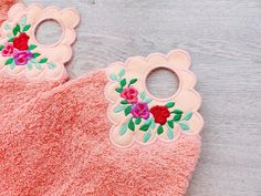 two baby bibs with flowers on them sitting on a wooden surface next to a pair of scissors