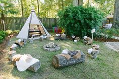 a teepee tent in the middle of a yard with logs and chairs around it