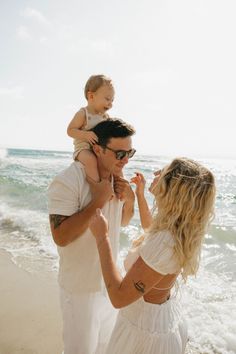 a man and woman holding a baby on the beach