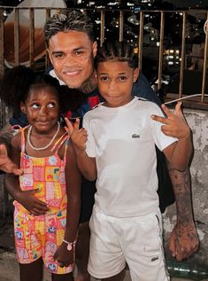 a man standing next to two children in front of a fence with his fingers up