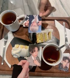 someone is holding up some photos on a tray with tea and cake