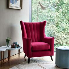 a red chair sitting in front of a window next to a table with a vase on it