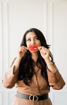 a woman in a brown dress is holding a red object up to her mouth