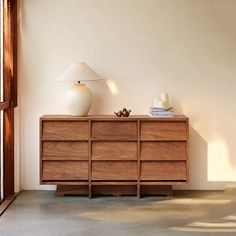 a white vase sitting on top of a wooden dresser next to a lamp and door