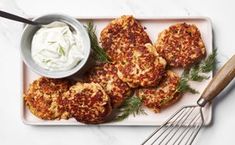 crab cakes on a plate with sour cream in a bowl and whisk next to it