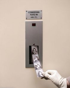 a person in white gloves is holding up a photo on a metal wall mounted elevator