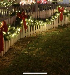 a white picket fence decorated with christmas lights and bows on the front yard at night