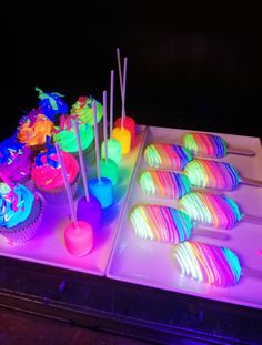 there are many cupcakes on the table with neon lights in the dark room