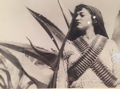 an old black and white photo of a woman with long braids standing in front of plants