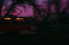 a red trolley car traveling down a street at night time with trees in the background