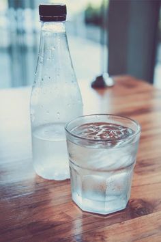 a glass and bottle of water sitting on a wooden table next to eachother