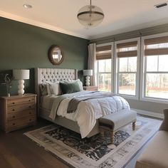 a bedroom with green walls and white bedding in the center, along with two windows