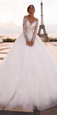 a woman standing in front of the eiffel tower wearing a white wedding dress