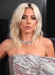 lady with blonde hair and silver dress posing in front of a black wall at an event