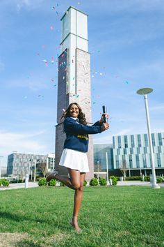 a woman in a blue jacket and white skirt is holding a cell phone while standing on the grass