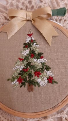 a cross stitch christmas tree with red and white flowers is on a tan surface, next to a green handled needle