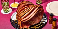 a large ham sitting on top of a black plate next to glasses and utensils