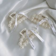 three pieces of pearls and ribbon on a white satin surface with the word love written across them