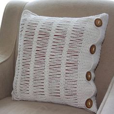 a crocheted pillow sitting on top of a beige chair next to a window