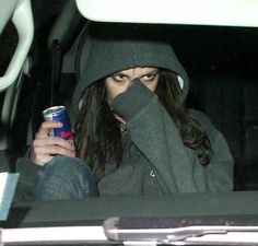 a woman sitting in the back of a car with a can of beer covering her face