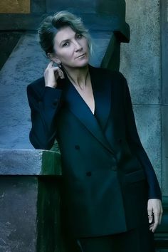 a woman wearing a black suit and holding a cell phone to her ear while standing in front of a wall