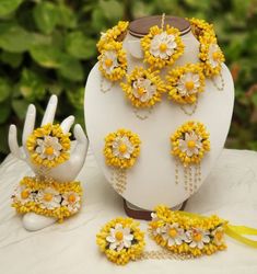 a white vase sitting on top of a table covered in yellow and white flowers next to jewelry