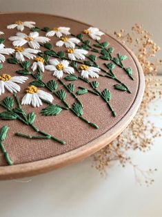 a close up of a embroidery on a wooden hoop with white and yellow daisies