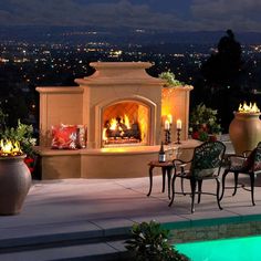 an outdoor fireplace in the middle of a patio with chairs and tables around it at night