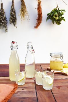 several bottles and glasses filled with liquid sitting on a wooden table next to some herbs