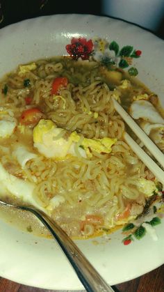 a white plate topped with noodles and vegetables next to a fork on top of a wooden table