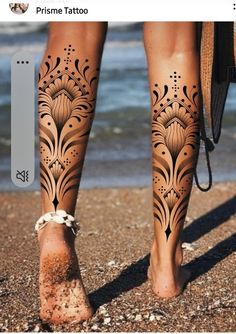 the legs and feet of a woman with hendix tattoos on them, standing in front of the ocean