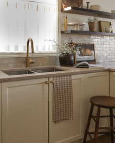 a kitchen with white cabinets and wooden stools next to an open shelf above the sink