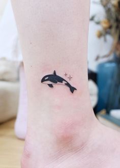 a small tattoo on the ankle of a woman with an orca whale and stars