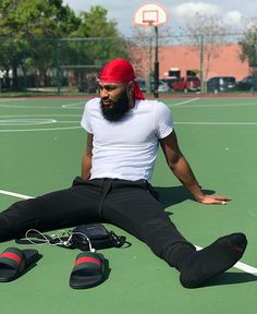 a man with a beard sitting on a tennis court wearing black pants and red bandanna