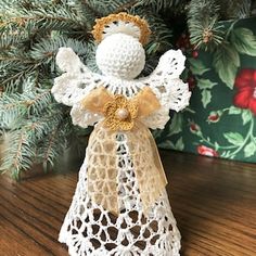 a crocheted angel ornament sitting on top of a table next to a christmas tree