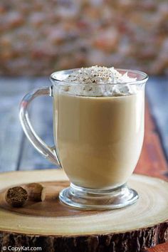 there is a cup of coffee with whipped cream in it on a wooden plate next to a piece of wood